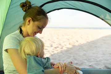 Fototapeta na wymiar Happy mom with child rest in the tourist tent. Sea and beach views