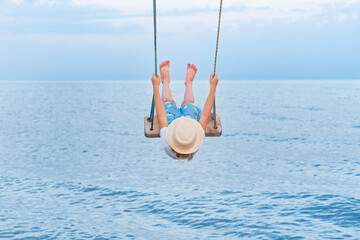 Child riding on rope swing over the water and lifted high legs. Vacation at sea with children