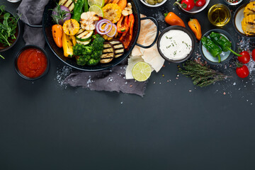 Grilled assorted vegetables in cast iron pan on black background.