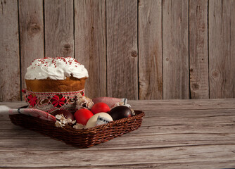Easter composition. Painted eggs, apricot flowers and a glazed Easter cake on a linen napkin in a basket on a wooden background. Happy Easter Holidays. Side view. Free space.
