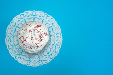 Easter composition. A glazed Easter cake with red sugar sprinkles on a white napkin is depicted in close-up on a pastel blue background. Happy Easter Holidays. Top view. Free space.