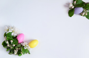 Easter composition. A border of blooming apple branches and colorful eggs on a white background. Happy Easter Holidays. Free space.