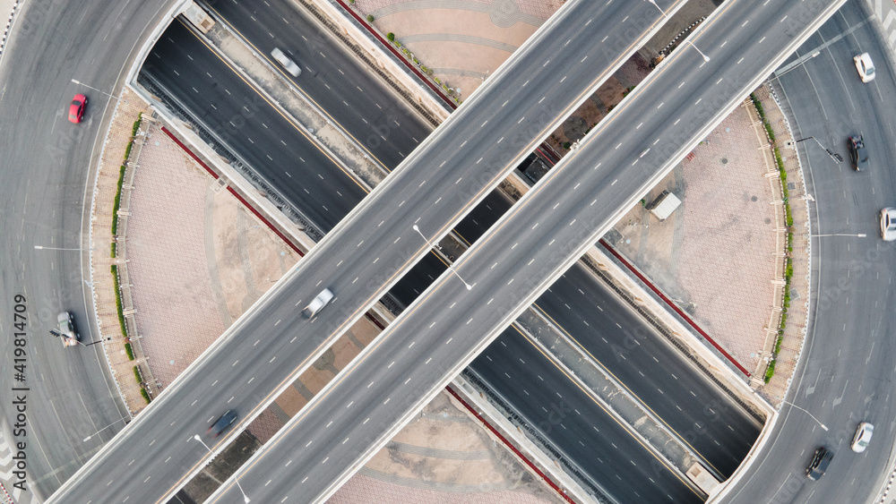 Wall mural Aerial view of road intersection with roundabout. Urban highway interchange with cars speeding. Junction network of transportation taken by drone. - Wall murals