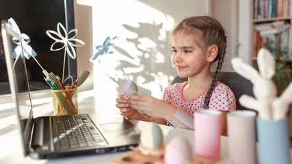 Girl demonstrating DIY flowers, wreath, eggs and greeting with spring holidays her family via internet, online Eater celebration, zero waste, craft for kids, new normal and social distance