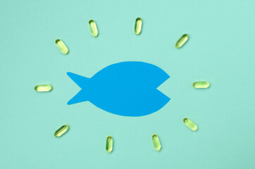 Top view of blue paper fish and yellow capsules of omega 3 on the blue surface