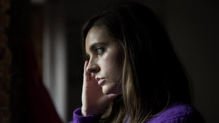 Anxious concerned woman standing by window looking outdoors thinking