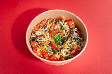Wok with udon noodles, vegetables, shitaki mushrooms, seaweed and chukka salad. Vegetarian food. In a food delivery plate. Close-up. View from above. Isolated.