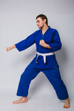 Young man in a blue kimono on a white background. The guy is a beginner in martial arts.