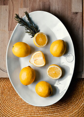 Lemons whole and cut in half, on a white plate, on wooden background