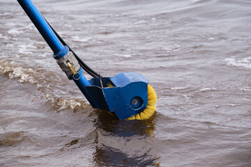 Device for automated collection of garbage, mud, spilled oil products from the water and the coastline, white brushes, against the background of water and sand of the reservoir