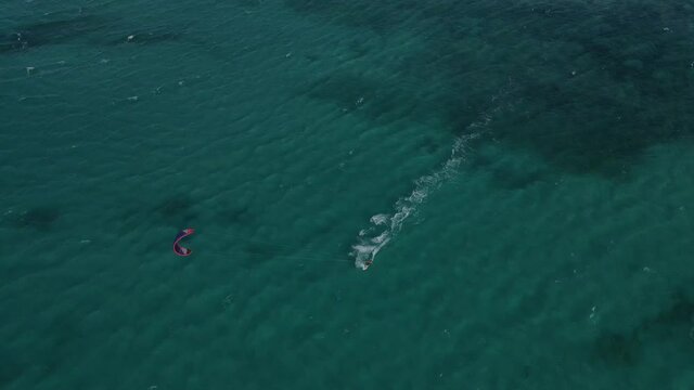 Aerial overhead flight showing kite surfer surfing on clear Pacific Ocean during beautiful weather outside.