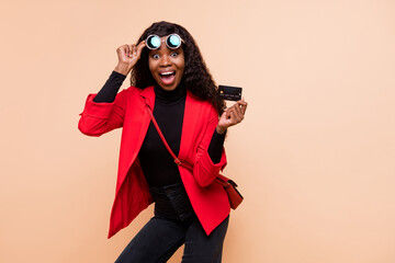 Photo of shocked brown haired afro american woman wear glasses hold debit card isolated on beige...