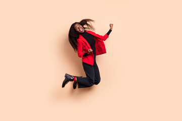 Fototapeta na wymiar Photo of lucky funny curly dark skin woman dressed red blazer jumping rising fists isolated beige color background