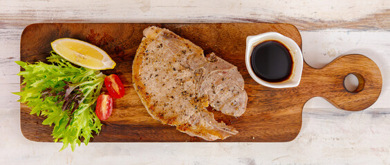 Pork steak with lemon and herbs on wood plate taken from top view