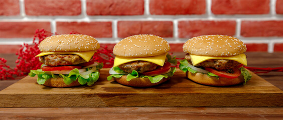 Set of three pork burgers on wooden plate in front of a brick background