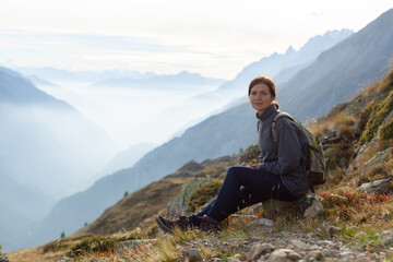 Woman with backpack enjoying sunset on peak of foggy mountain. Tourist traveler on background view mockup. Hiker looking sunlight in trip in Italy country mock up text. Alpine mountain