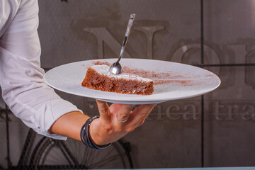 Piatto con fetta di torta caprese con cucchiaino mantenuto da un cameriere