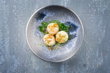 Modern style fried scallops with crumbles and lemon slices served with kalette cilanto relish as top view on a Nordic design plate with copy space