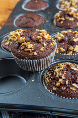 Close up on a healthy gluten free chocolate muffin with walnuts. Homemade, freshly baked goods with cocoa powder and dark chocolate placed in a muffins tray on a wooden background. Nutrition concept.