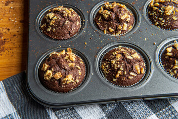 Healthy gluten free chocolate muffins with walnuts. Homemade, freshly baked goods with cocoa powder and dark chocolate placed in a muffin tray on a wooden background. Nutrition concept.
