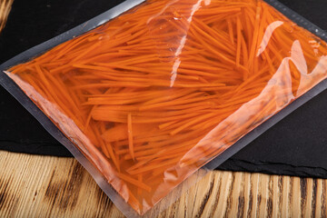Sliced fresh carrots in big vacuum sealed plastic bag on black slate board