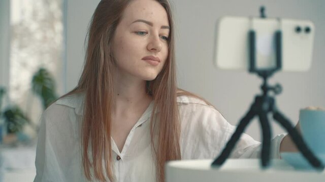 Streamer at home. Portrait of young female artist female doing live streaming with a smartphone and drawing with a tablet.