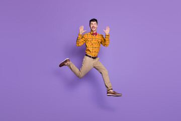 Full length photo of young excited man happy positives mile jump up wave hello isolated over purple color background