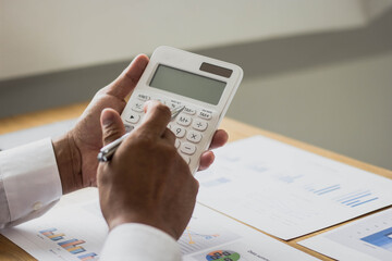 A businessman is using a calculator to calculate monthly company income figures in financial documents, he is summarizing financial data to bring to meetings with business partners. Financial concept.