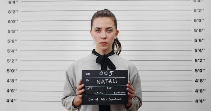 Portrait of young woman with ponytail holding sign for photo in police department. Crop view of pretty female criminal posing, raising head and looking to camera.Concept of mugshot.