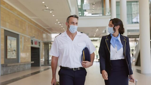 Airliner pilot and air hostess wearing face mask walking in airport terminal during the covid pandemic.