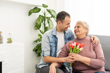 Lovely son coming home and carrying bouquet of flowers to his mother