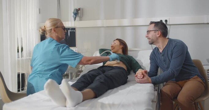 Mature pregnant couple smiling looking at the sonogram results on ultrasound scanner monitor