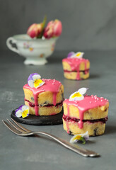 kleine Napfkuchen mit Himbeerfüllung und Himbeerglasur, dekoriert mit Zuckerperlen und Hornveilchen