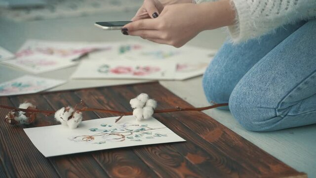 Young female creator taking photos of her illustrations. Close-up.