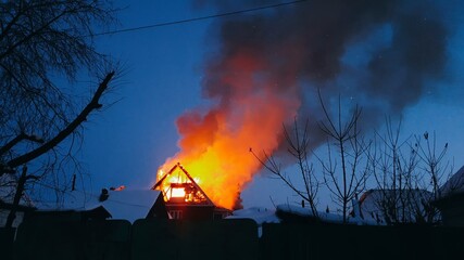 The roof of the house is on fire. The residential building burn, village. Firefighters put out a fire from the crane from above. The fire Department putting out the open flame. Smoke and sparks.