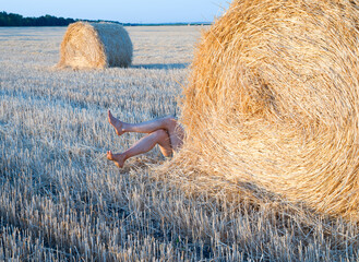 the legs of a lying man stick out from behind a bale of straw on the field