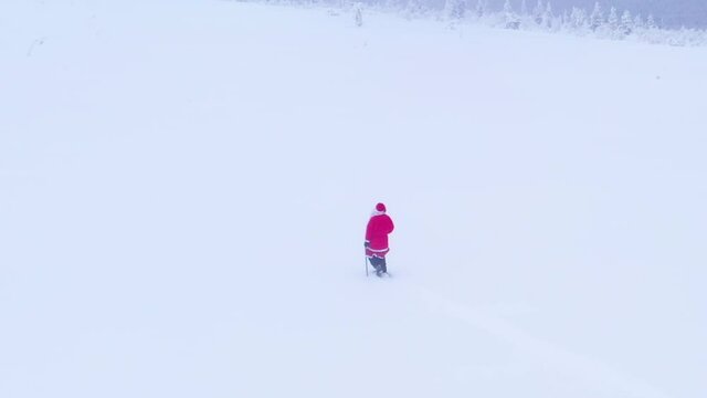 Aerial drone view following Santa Claus walking on a snowy mountain, gloomy, winter blizzard, in Lapland