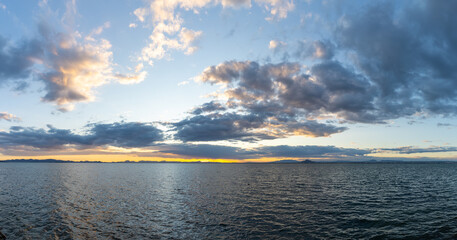 calm ocean waters under an expressive sky at sunset with mountain silhouette in the background