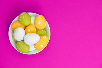 Colored eggs in a white plate on a pink background. Easter eggs. Copy space. Spring mood with yellow, white and green chicken eggs. 