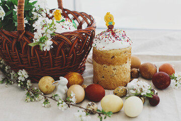 Homemade Easter bread, modern eggs, basket, bunny and blooming spring flowers on rustic table