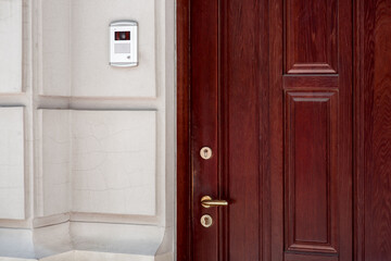 brown wooden front door cracked stone facade light building exterior with intercom for security...