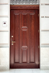 brown wooden front door stone facade building exterior with intercom for security with video camera...