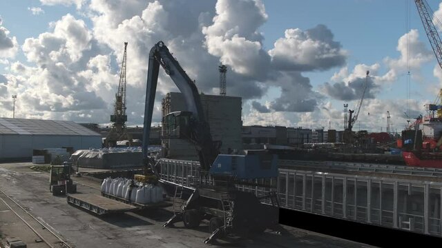 large metal crane puts white bags with mineral fertilisers on steamboat deck in local harbour under cloudy sky timelapse
