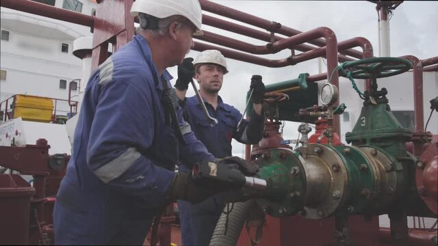 skilled engineers repair oil tanker pipeline of green and silver colours near large valve under white cloudy sky