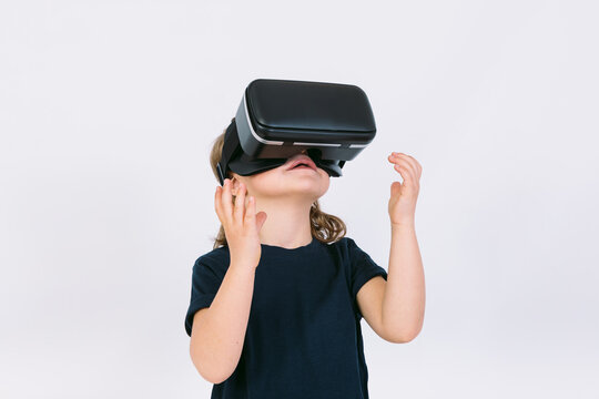 Little girl with virtual reality glasses looking up on white background