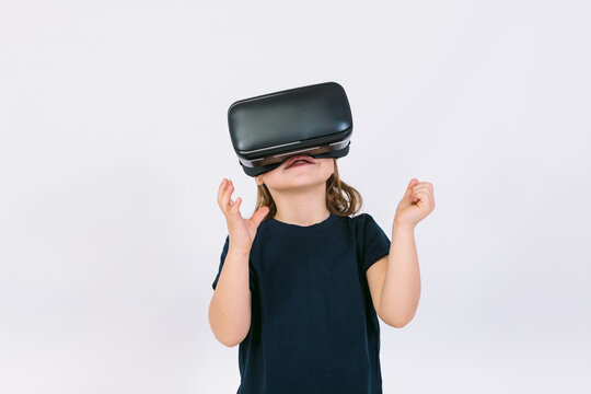 Little girl wearing virtual reality glasses with hands trying to touch something virtually, on white background