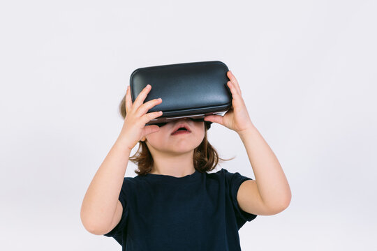 Little girl with virtual reality glasses looking up on white background