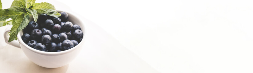 Ripe blueberry and green leaves in white cup on a light background