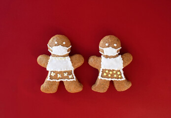 Cute gingerbread women with protective face masks on red background, coronavirus (COVID-19) time