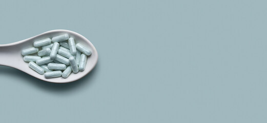 Website header with white tablespoon filled with clear capsules with blue powder on mint background.